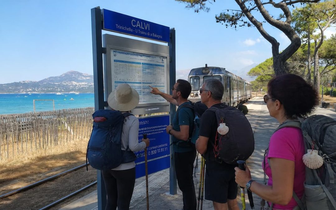 Gruppo di pellegrini con zaini consulta gli orari del treno Trinichellu alla stazione di Calvi in Corsica, lungo il Cammino di Santa Giulia