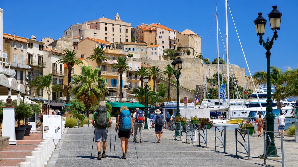 Pellegrini con zaino camminano sul lungomare di Calvi davanti al porto e alla cittadella in Corsica lungo il Cammino di Santa Giulia